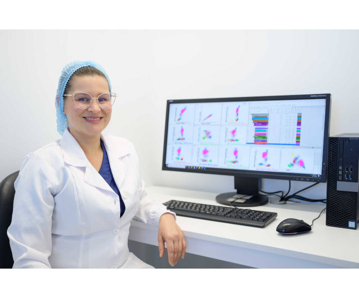 Se visualiza imágen de una doctora sonriendo, en el fondo una computadora con resultados de exámenes en su pantalla