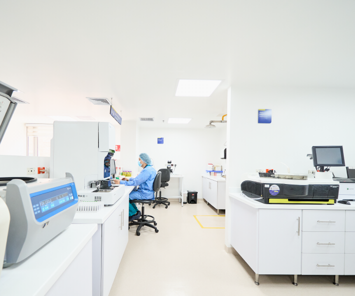 Se observa vista panorámica de un laboratorio en el cual se encuentran escritorios, equipo médico y un profesional de la salud sentado frente a la computadora.