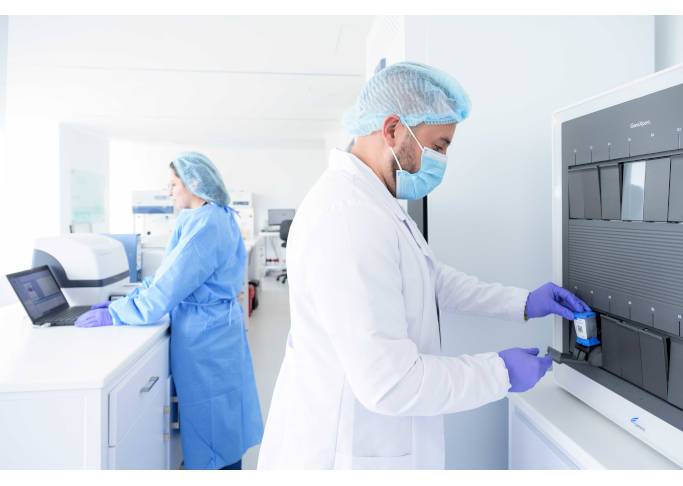 En un ambiente de laboratorio hay dos profesionales de la salud de pie, manipulando equipo médico.