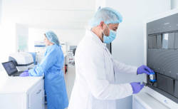 En un ambiente de laboratorio hay dos profesionales de la salud de pie, manipulando equipo médico. 