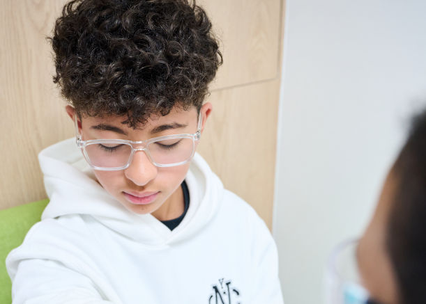 Un adolescente con gafas se encuentra sentado con expresión tranquila en una sala de espera.