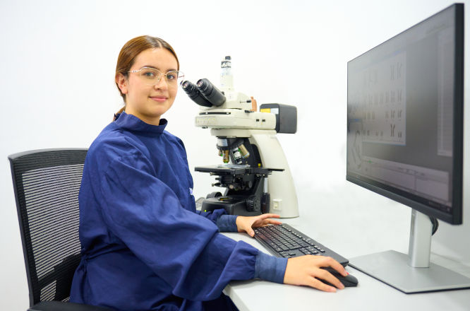 Una doctora se encuentra sentada en su escritorio frente a una pantalla de computadora mirando hacia el frente.